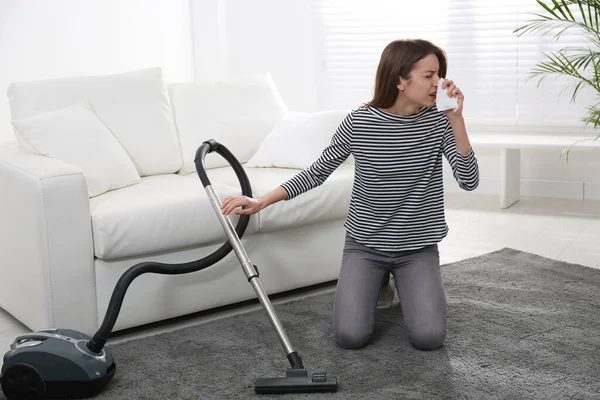 Young woman suffering from dust allergy while vacuuming house
