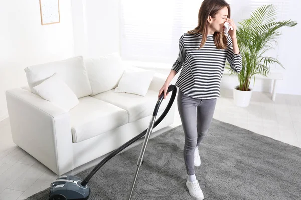 Young woman suffering from dust allergy while vacuuming house