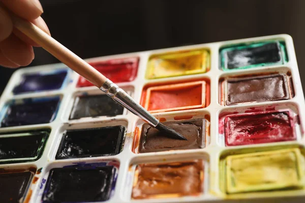 Woman holding brush and watercolor palette, closeup