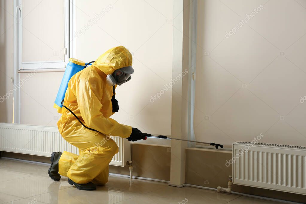 Pest control worker in protective suit spraying pesticide indoors. Space for text