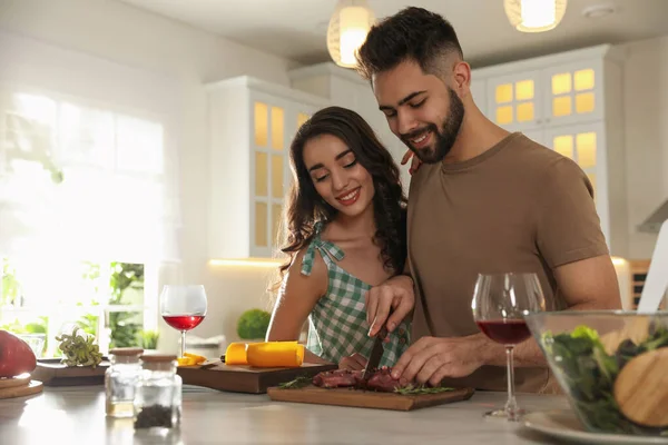 Lovely young couple cooking meat together in kitchen