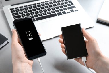 Cep telefonunu elektrik bankasıyla yükleyen kadın açık gri taş masada, yakın plan.