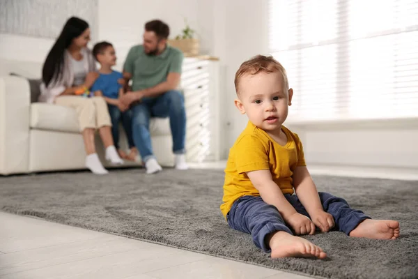 不幸的婴儿独自坐在地板上 而父母则与他的哥哥呆在家里 家庭中的嫉妒 — 图库照片