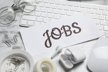 Kelime JoBS, bilgisayar klavyesi, kulaklıklar ve beyaz mermer masadaki kırtasiye malzemeleri. Kariyer konsepti