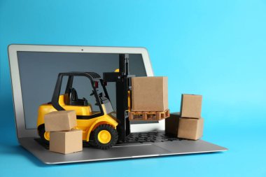 Laptop, forklift modeli ve açık mavi arkaplanda karton kutular. Kurye servisi