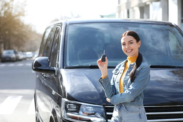 Young woman with key near car on city street. Buying new auto