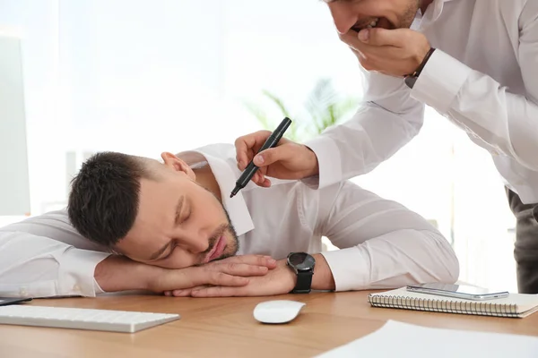 Man drawing on colleague\'s face while he sleeping at workplace. April fool\'s day
