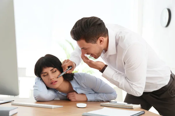 Man drawing on colleague's face while she sleeping at workplace. April fool's day