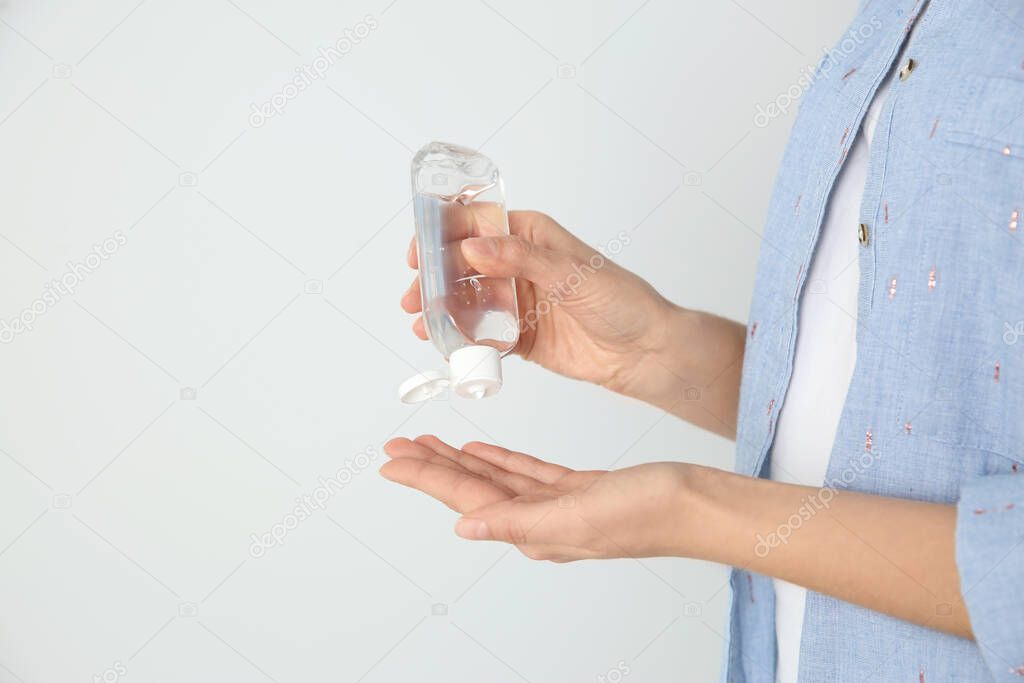 Woman applying antiseptic gel on light background, closeup