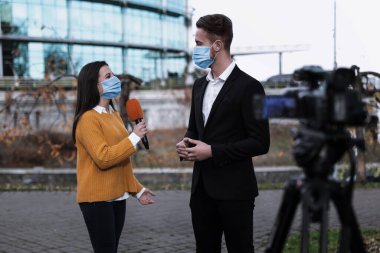 Dışarıda tıbbi maskeli genç bir gazeteci ve iş adamı var. Virüs koruması