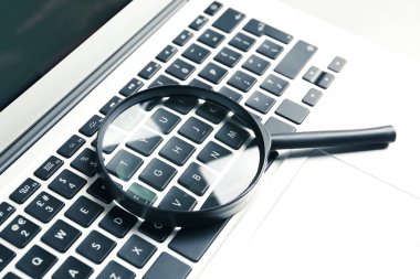 Büyüteç ve modern laptop masada, yakın plan. Arama konsepti