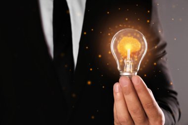 Gri arka planda parlak beyinli ampulü tutan adam, yakın plan. Fikir oluşturma