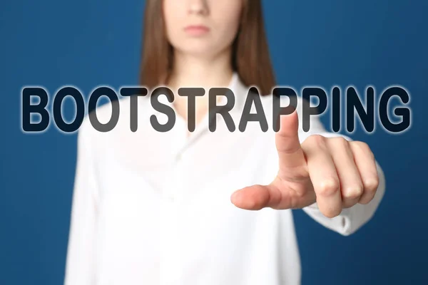 Woman touching virtual screen with word BOOTSTRAPPING against blue background, focus on hand