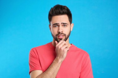 Açık mavi arka plandaki dalgın genç adam. Zor soruyu düşünüyorum.