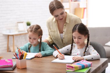 Anne, içeride kızlarına ev ödevlerinde yardım ediyor.