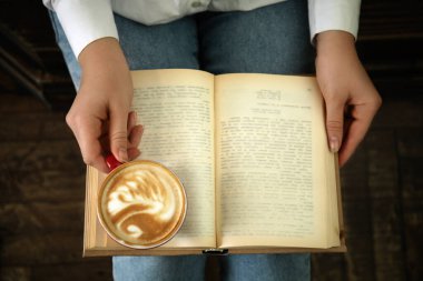 Bir fincan kahve içip kitap okuyan bir kadın.