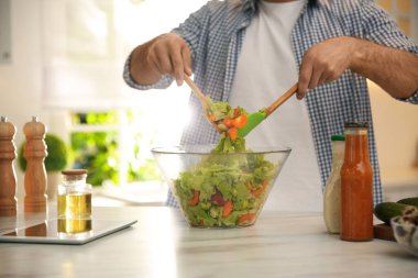 Mutfaktaki masada tabletli bir adam salata pişiriyor.
