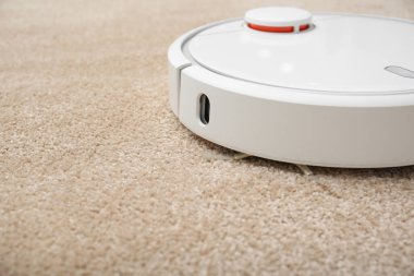 Kapalı alanda modern robot süpürgeyle halıdaki toprağı temizlemek.