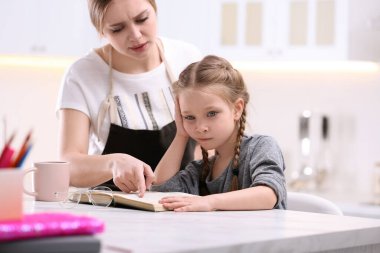Woman helping her daughter with homework at table in kitchen clipart