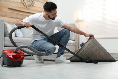 Evde elektrikli süpürge kullanan genç bir adam.