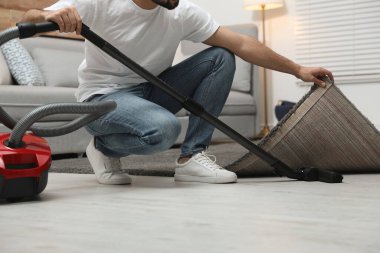 Evde elektrikli süpürge kullanan genç adam, yakın plan.