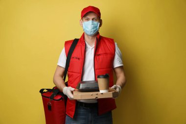 Sarı arka planda koruyucu eldivenli ve maske takan kurye. Coronavirus karantinası sırasında yiyecek teslimatı