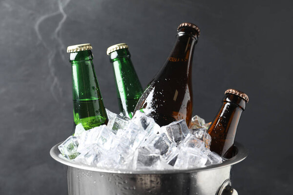 Metal bucket with bottles of beer and ice cubes on grey background