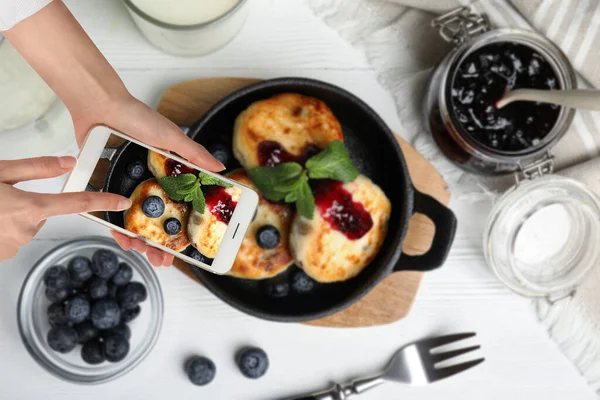 Food blogger taking picture of delicious cottage cheese pancakes at white wooden table, closeup