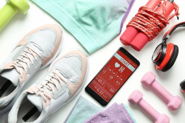 Beyaz arka planda fitness uygulaması ve spor aksesuarları olan akıllı telefon, düz uzanma