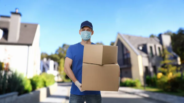 Courier in protective mask and gloves with boxes on street. Delivery service during coronavirus quarantine