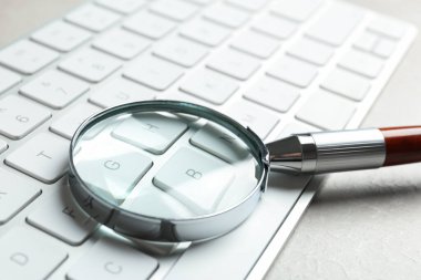 Açık gri mermer masa üzerinde büyüteç ve bilgisayar klavyesi, yakın plan. Arama konsepti