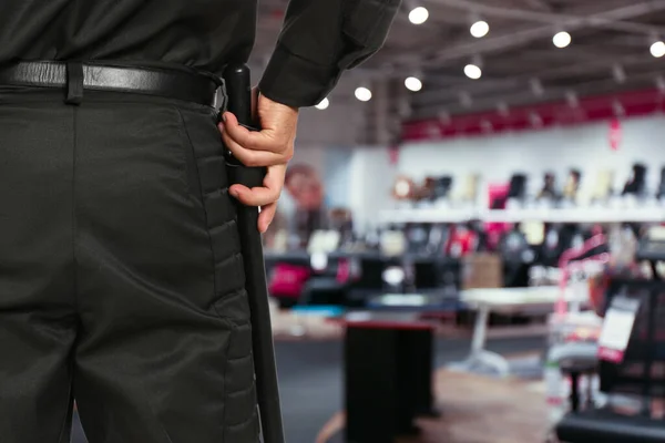Security guard in uniform with police baton in shopping mall, closeup. Space for text