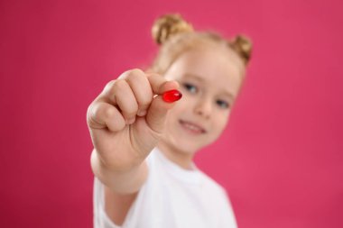 Pembe arka planda vitamin hapı kullanan küçük kız, eline odaklan.