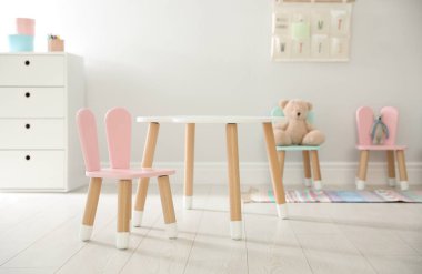 Küçük masa ve içinde tavşan kulağı olan pembe sandalye. Çocuk odasının içi.