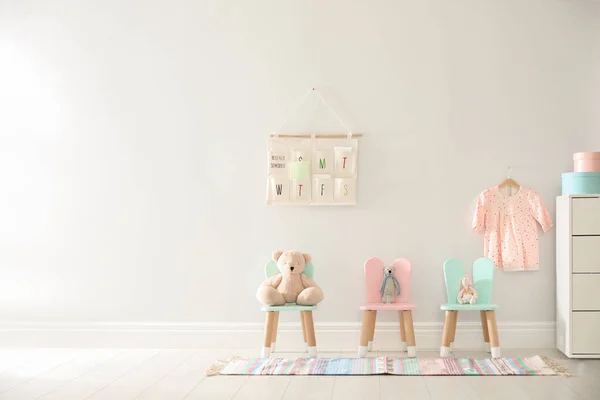 Cute toys on chairs with bunny ears near white wall indoors, space for text. Children's room interior