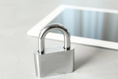 Açık gri masada metal kilit ve tablet, yakın plan. Siber saldırılara karşı koruma