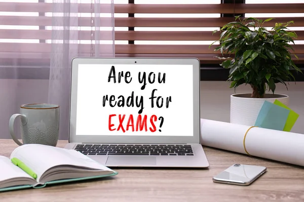 Laptop with phrase ARE YOU READY FOR EXAMS on wooden table in office
