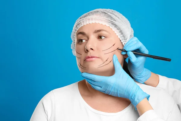 Lekarz Rysujący Ślady Twarzy Kobiety Podczas Operacji Plastycznej Niebieskim Tle — Zdjęcie stockowe