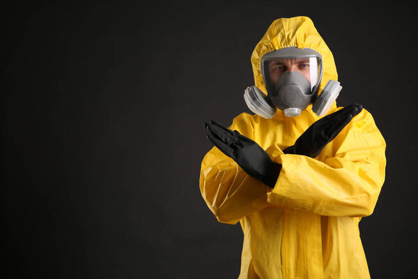 Man in chemical protective suit making stop gesture on black background, space for text. Virus research