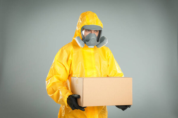 Man wearing chemical protective suit with cardboard box on light grey background. Prevention of virus spread