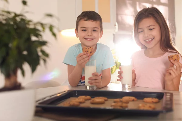 Cute little children eating cookies with milk in kitchen. Cooking pastry