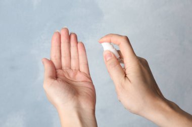 Açık mavi arka planda kadının eline antiseptik püskürtüyor. Yakın plan. Virüs önleme
