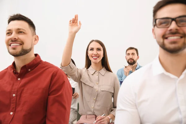 Young woman raising hand to ask question at business training on white background