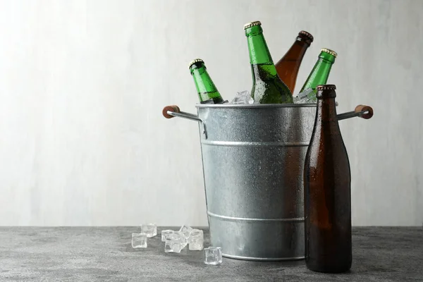 Metal bucket with beer and ice cubes on grey background. Space for text