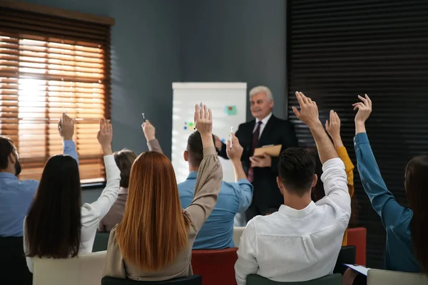 People raising hands to ask questions at seminar in office