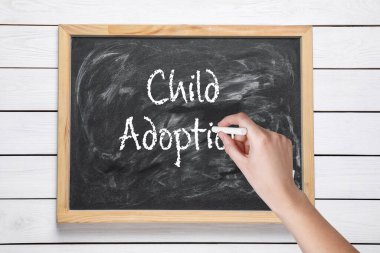 Beyaz ahşap arka planda ÇOCUK ADOPTION ifadesini yazan kadın, yakın plan