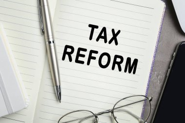 Sözcükler içeren defter: Vergi REform, masa üzerinde kalem ve gözlük, yakın plan