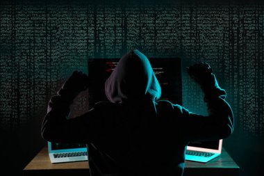 Karanlık odadaki bilgisayarların yanındaki hackerlar ve arka plandaki dijital semboller. Sanal suç kavramı
