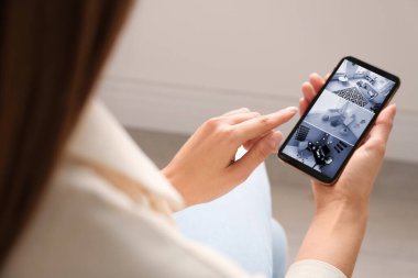 Modern mobese kameralarını izleyen bir kadın akıllı telefondan kapalı alanda, yakın plan. Ev güvenlik sistemi