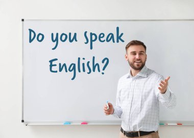 Sınıfta beyaz tahtanın yanında genç İngilizce öğretmeni